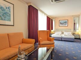 Orangefarbene Couch neben einem Sessel unter einem blauen Gemälde gegenüber von dem großzügigen Doppelbett 