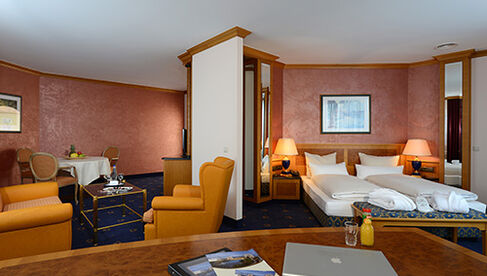 Großzügiges Zimmer mit Schreibtischen, Doppelbett, gelben Sesseln und Tisch mit zwei Stühlen 