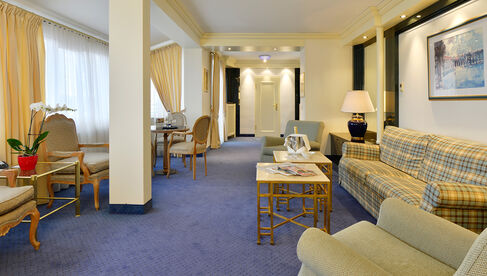 Wohnbereich mit karierter Couch zwischen zwei grauen Sesseln auf blauem Teppichboden