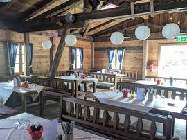 Licht fällt durch eine offene Tür in die Almhütte mit gedeckten Tischen 